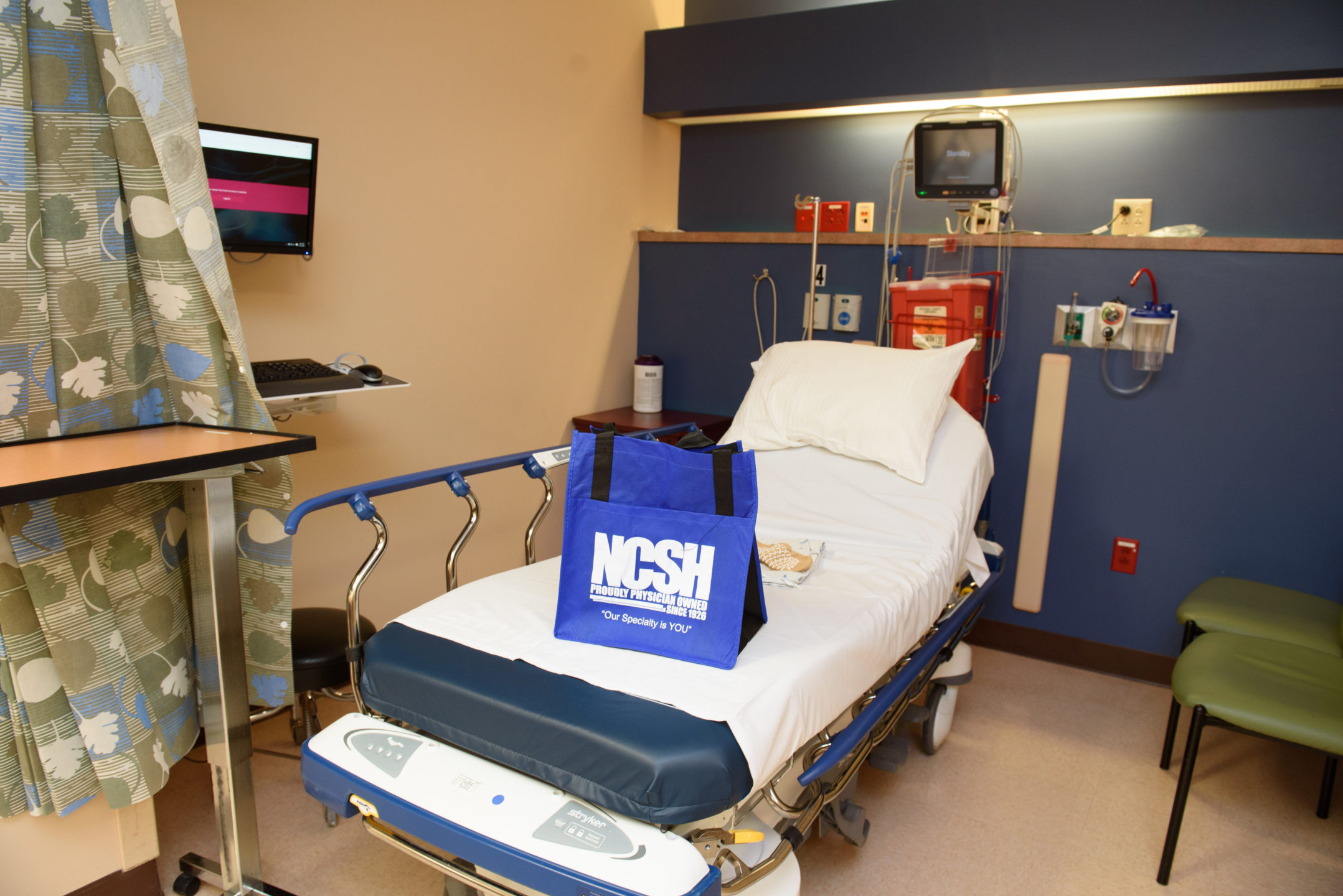 A bag with North Carolina Specialty Hospital branding sits at the end of a hospital bed