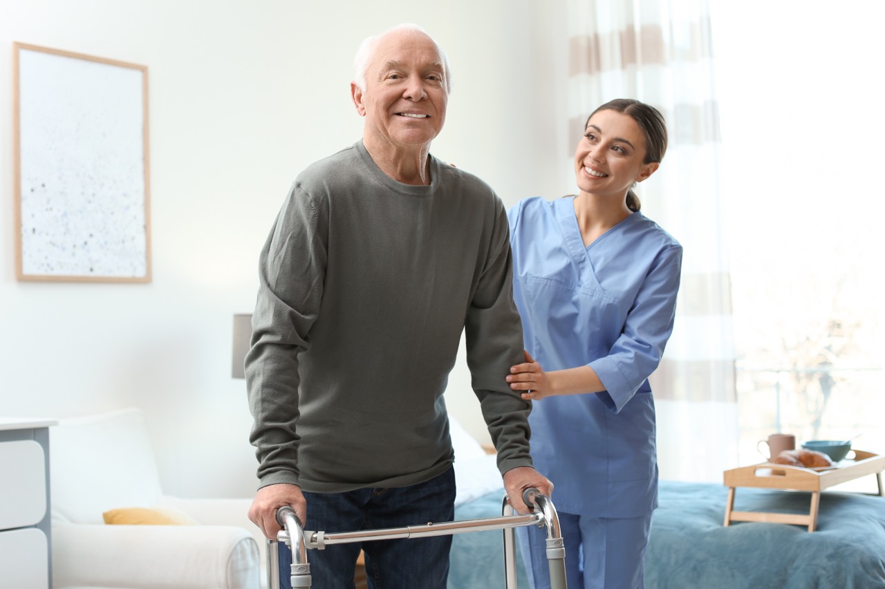 A nurse helps an older male patient walk with a walker as he recovers from hip replacement.