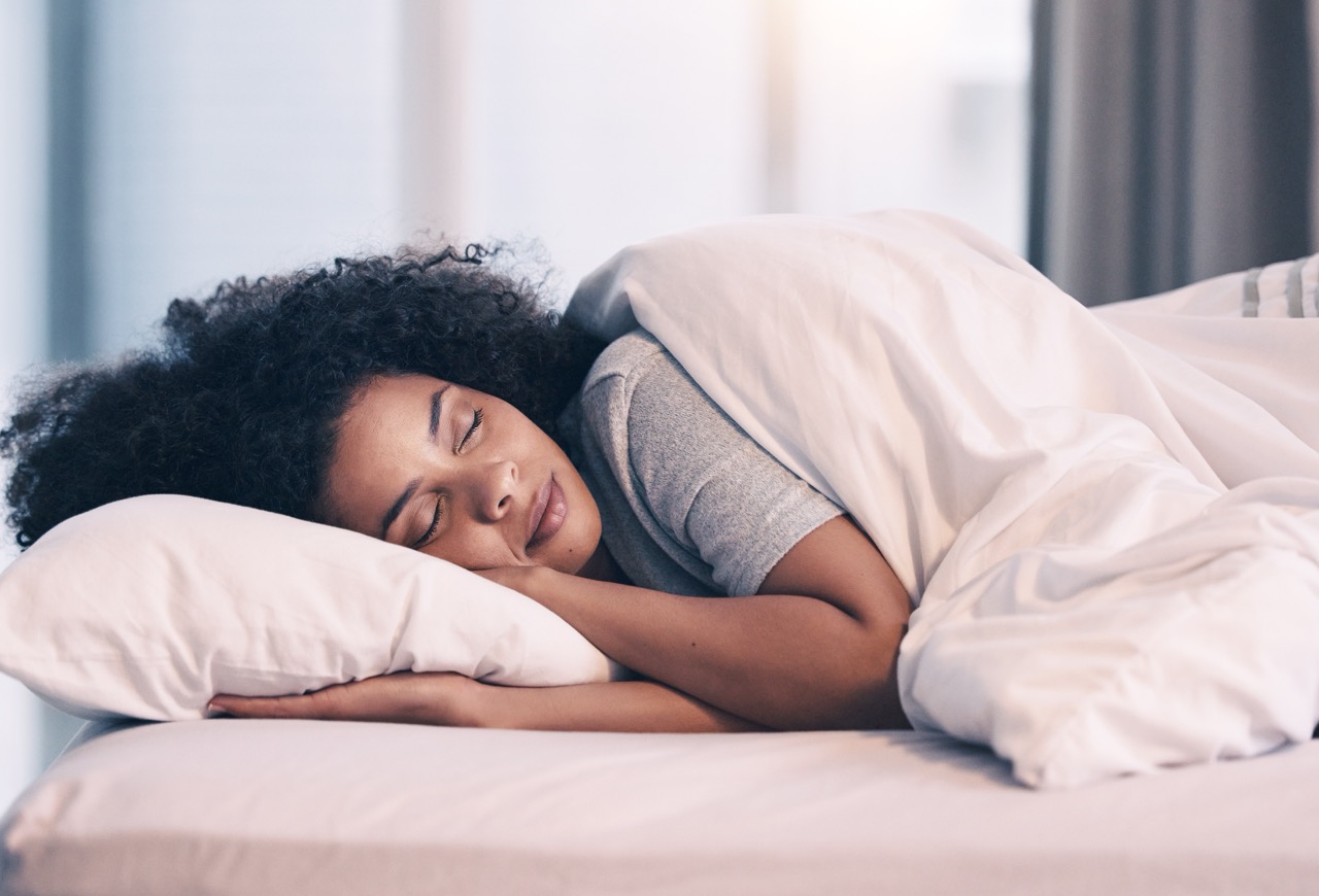 A young woman sleeps on her side, the best kidney stone pain relief position.