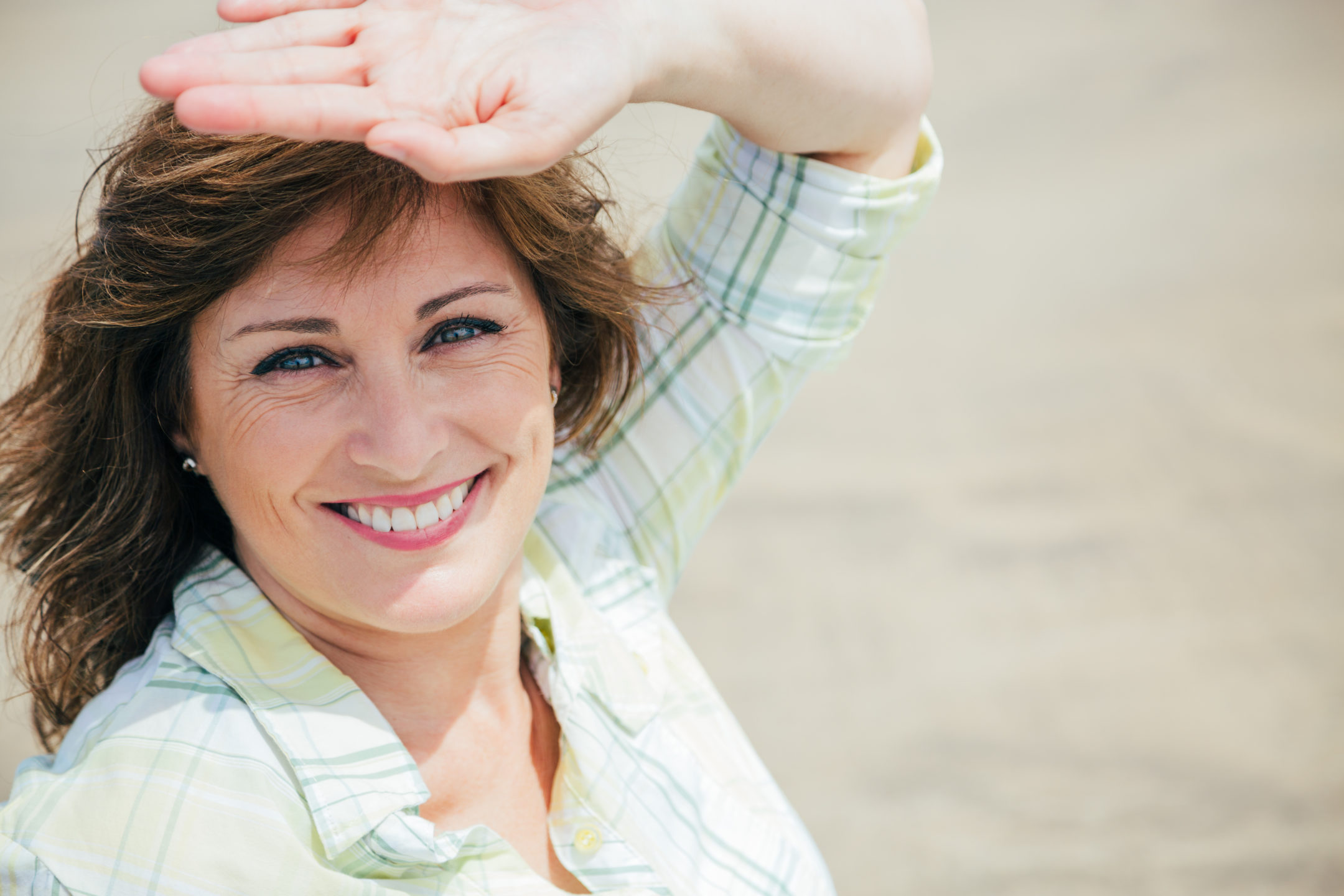  A middle-aged woman with her hand held up to shade the sun from her eyes considers breast reduction surgery in NC.