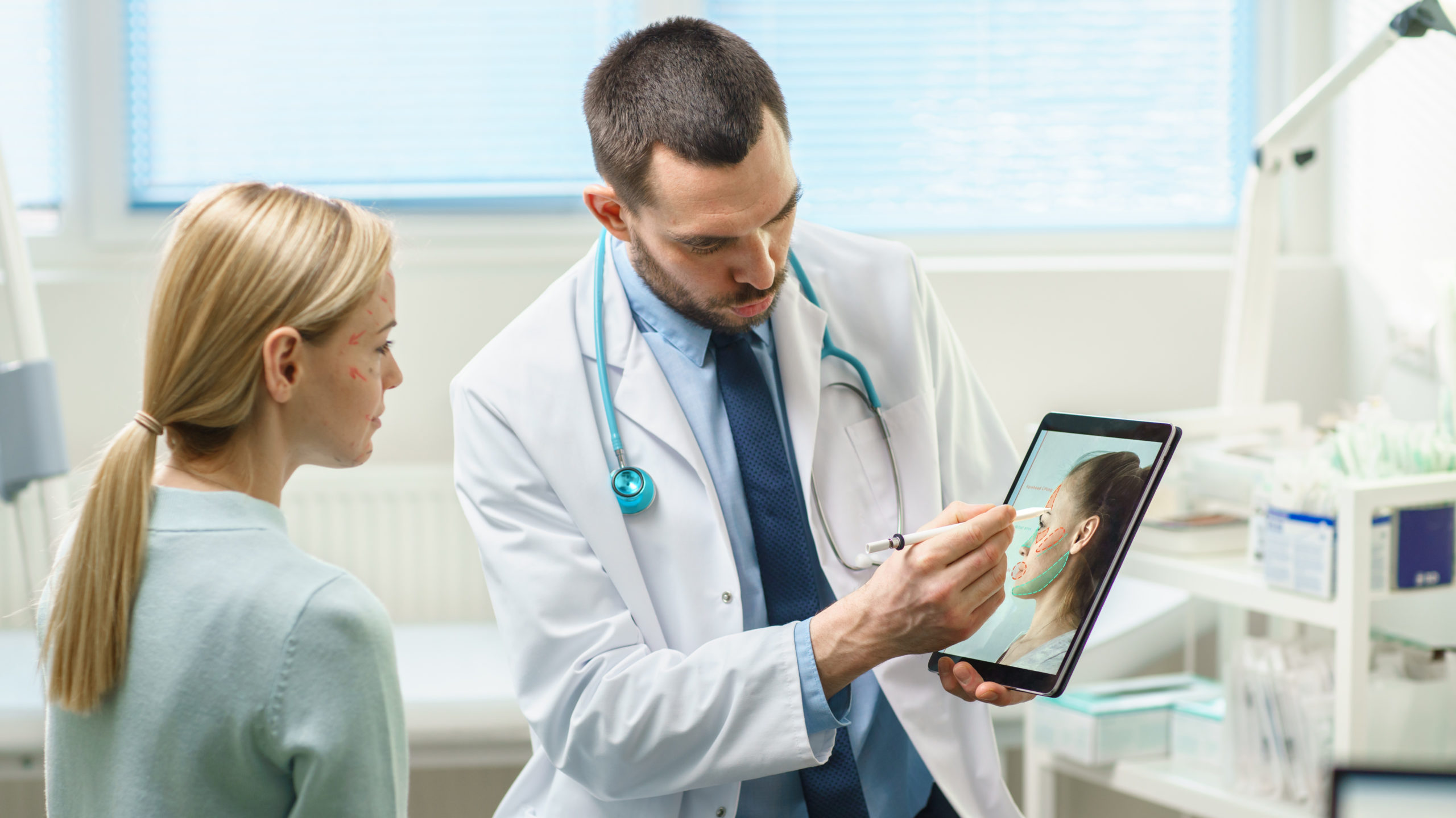A plastic surgeon explains a procedure to a patient using a tablet. 