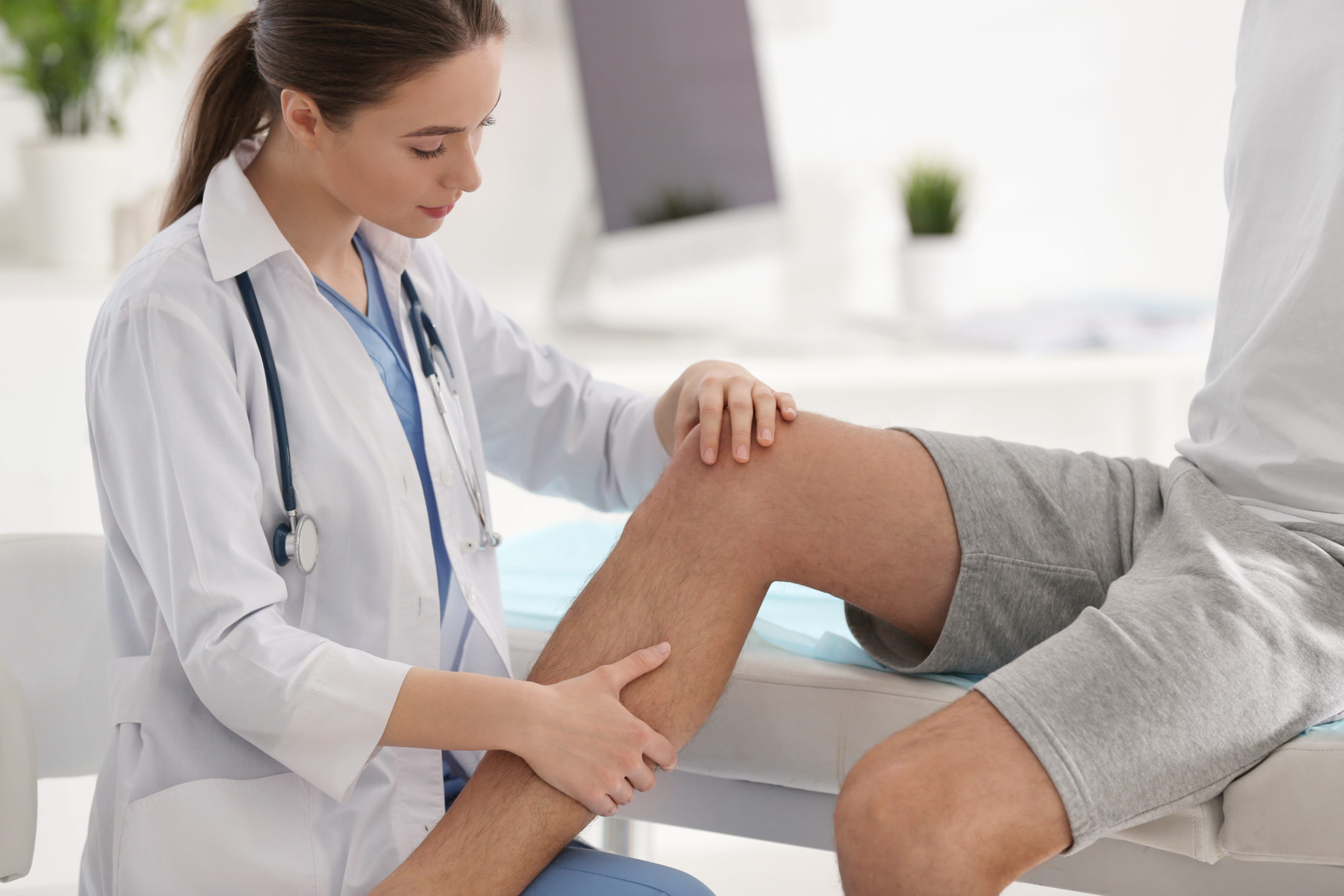 A young woman surgeon examines a man’s knee for partial knee replacement surgery. 