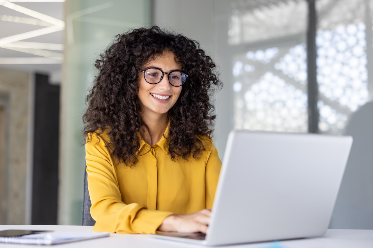 A girl wearing glasses smiles as she works on her computer, no longer suffering from eye strain.