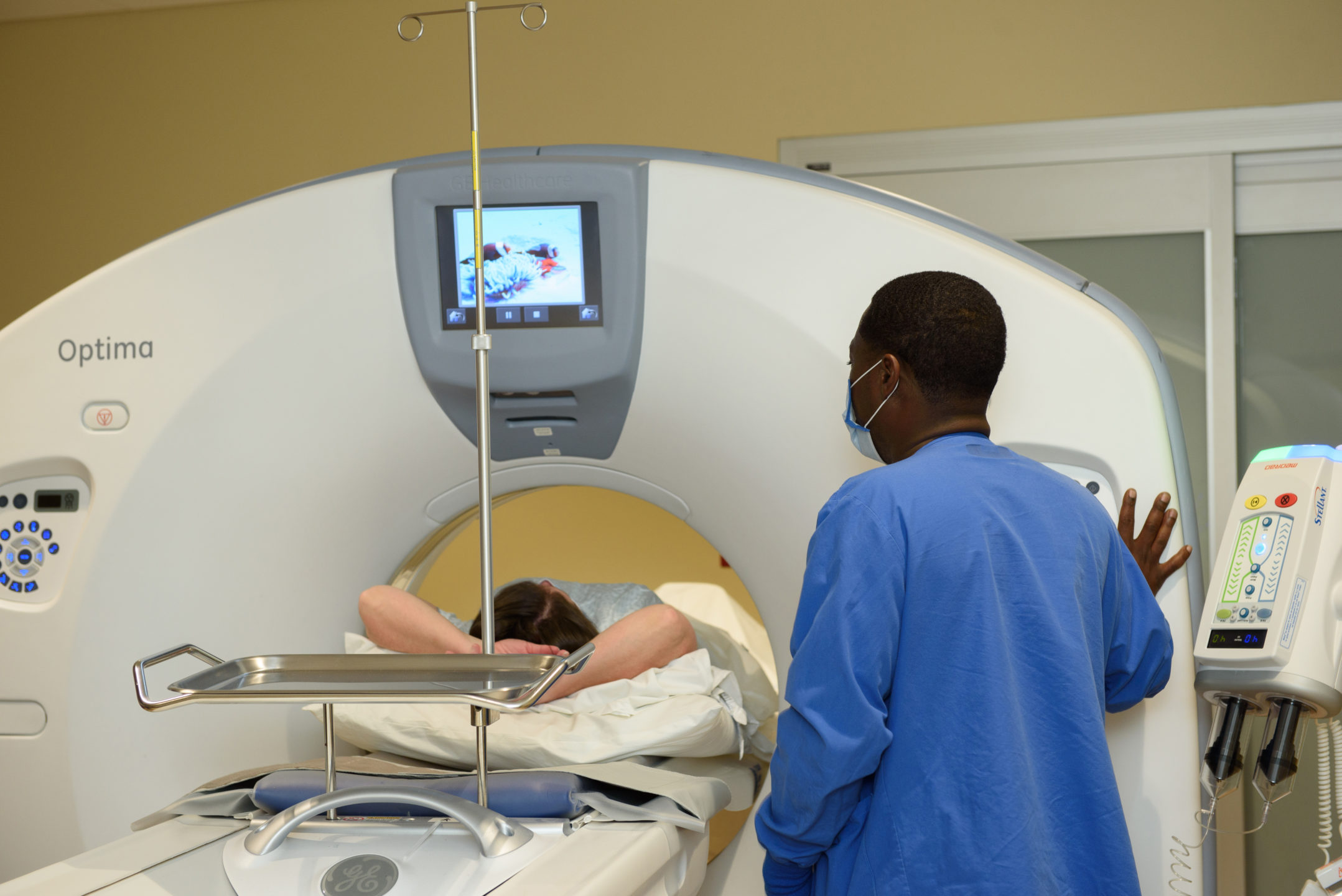 A technician assists a patient and operates a CT scanner. 