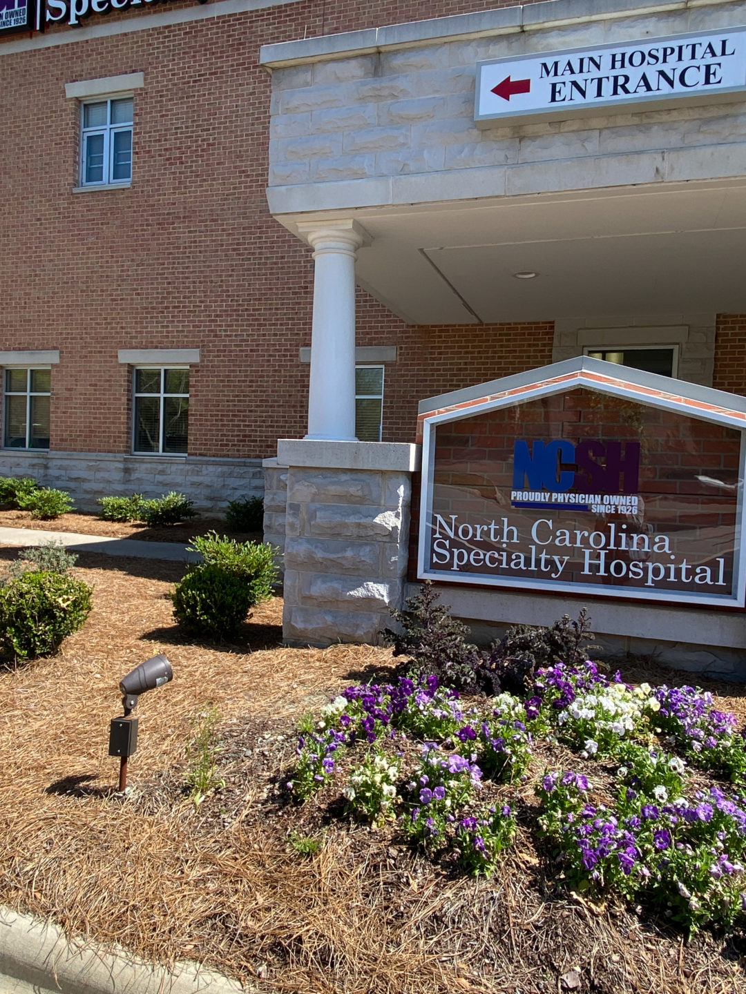 The exterior of the building shows the North Carolina Specialty Hospital sign surrounded by flowers. 