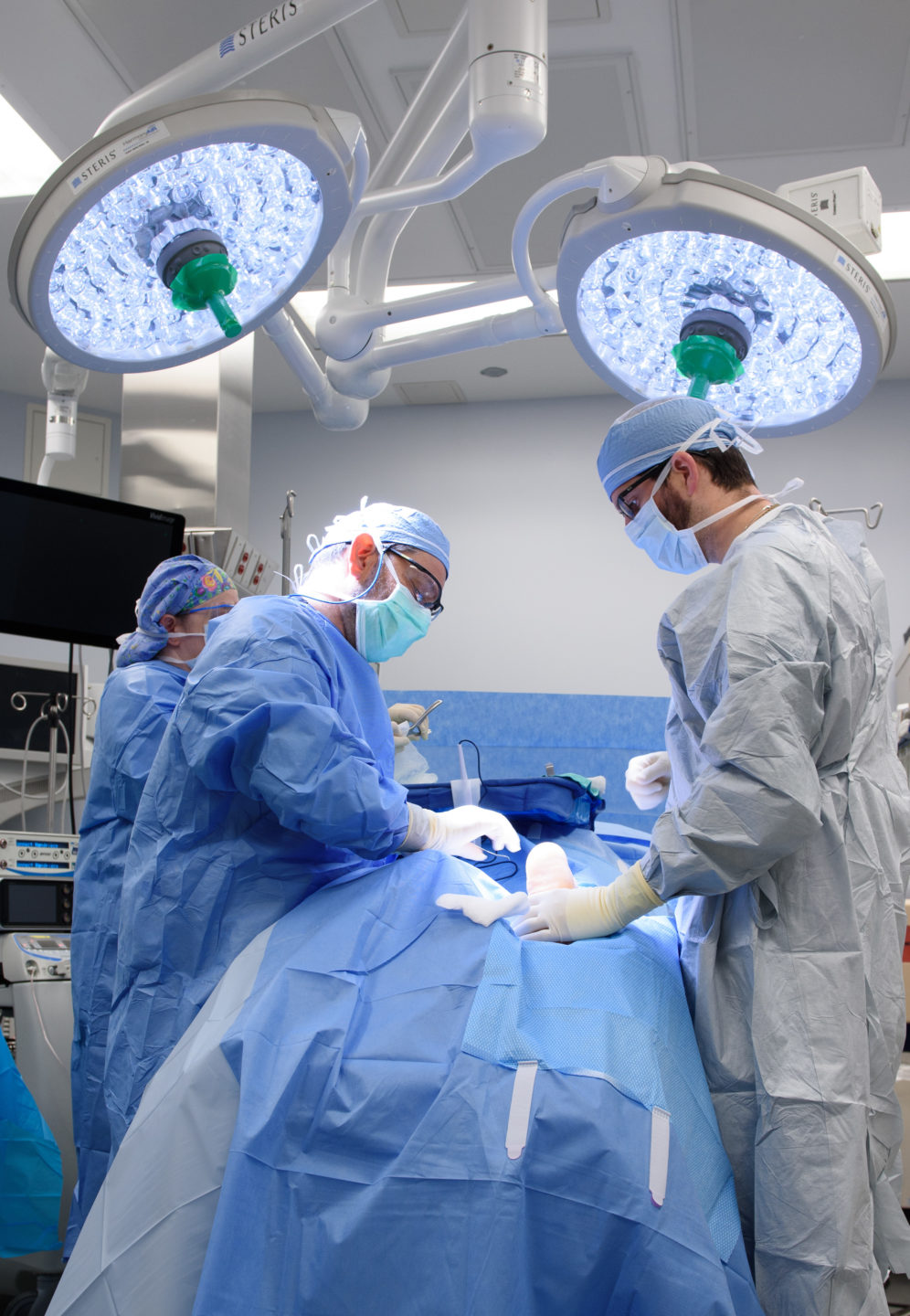  A surgeon and two assistants operate on a patient’s foot in an operating room. 