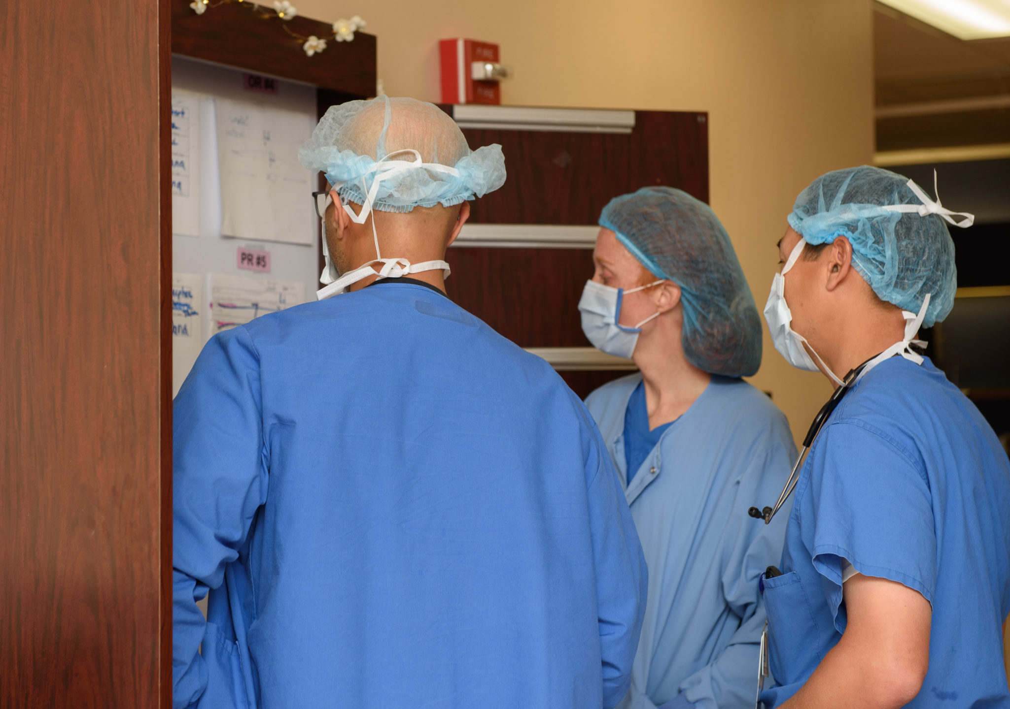  Three surgery staff members in masks stand and go over patient charts. 