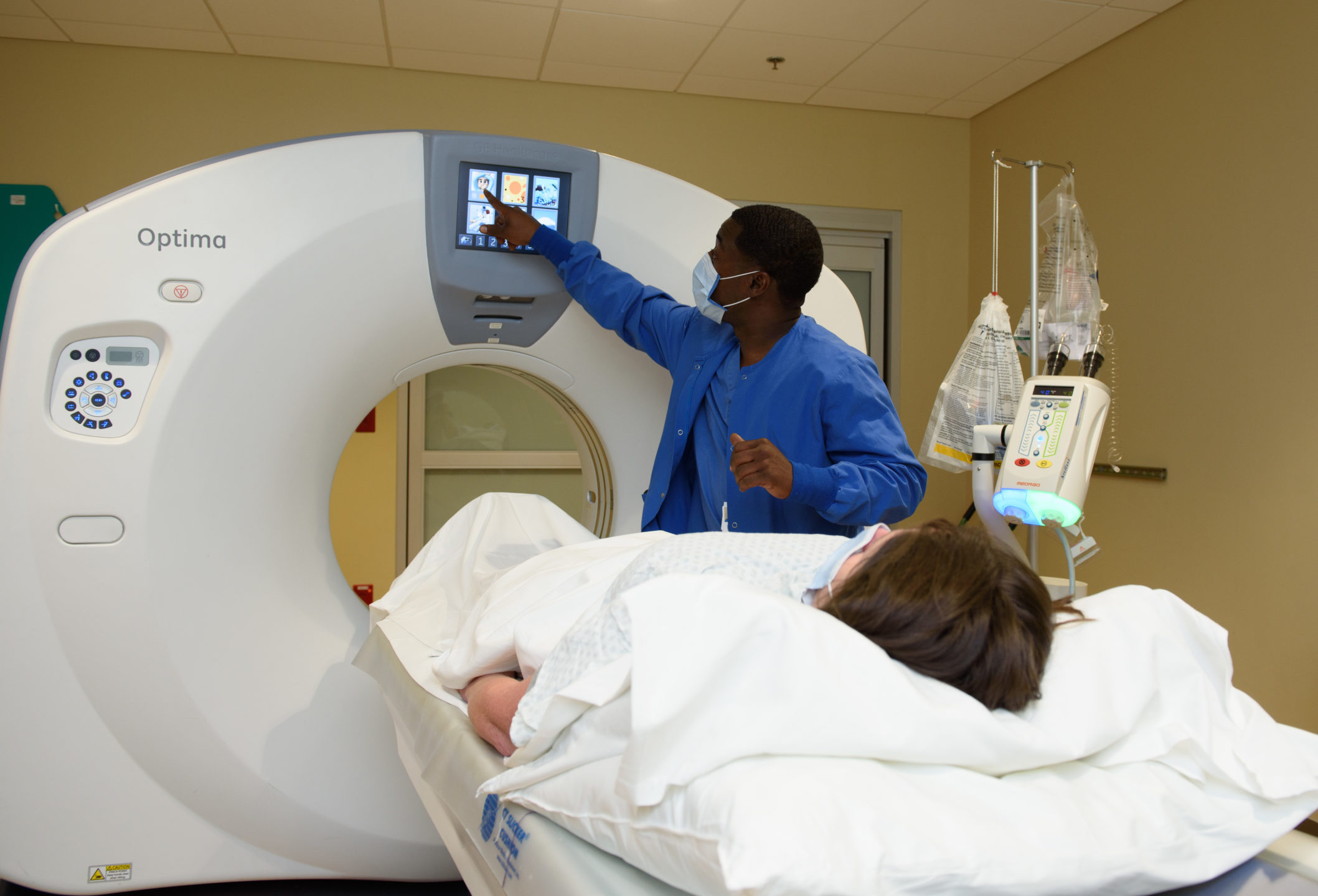 A radiology tech points to a screen as a patient prepares to enter the CT machine. 