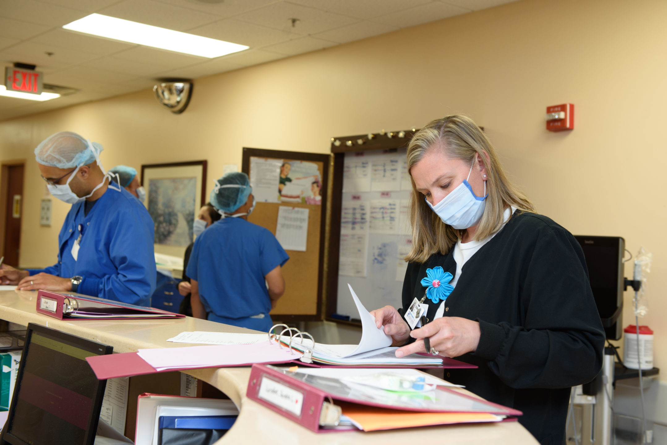 Staff members go through paperwork at a desk while others review schedules in the background. 