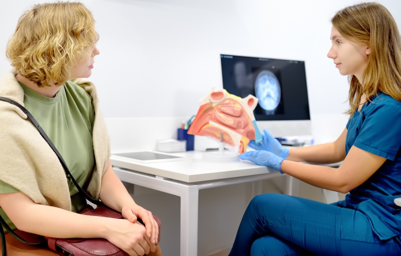 A doctor shows a cross-section model of a nose to a woman with a deviated septum.