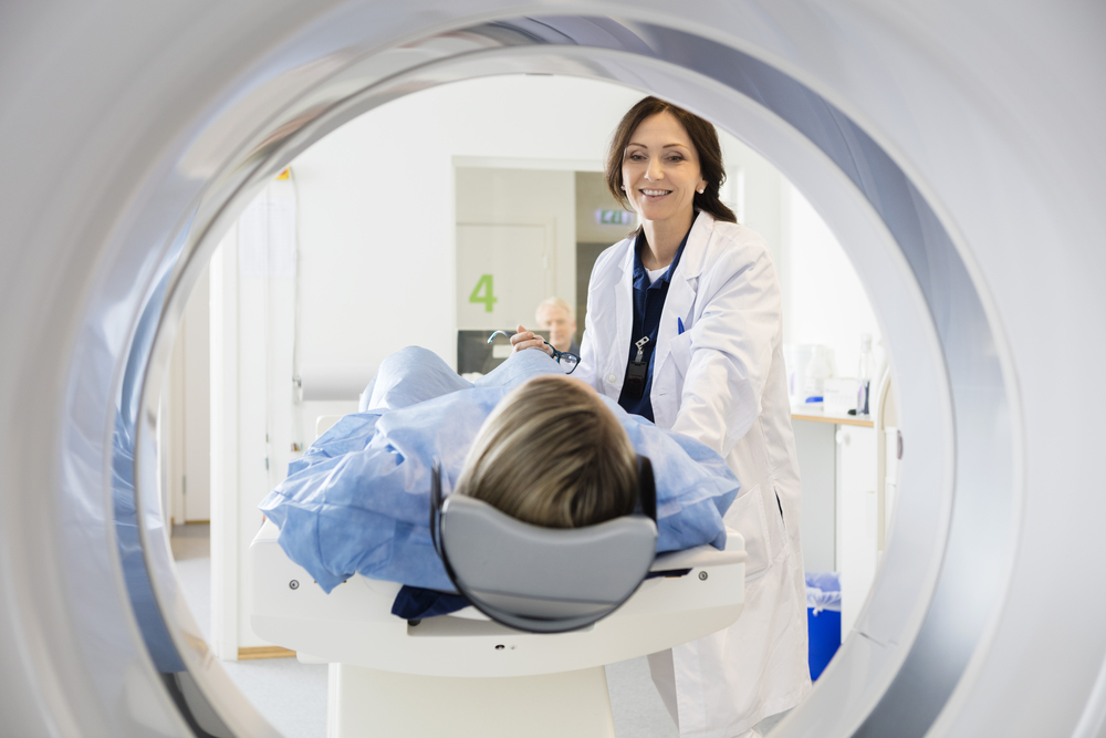 An NCSH technician stands next to a patient who is entering a CT scanner for medical images. 