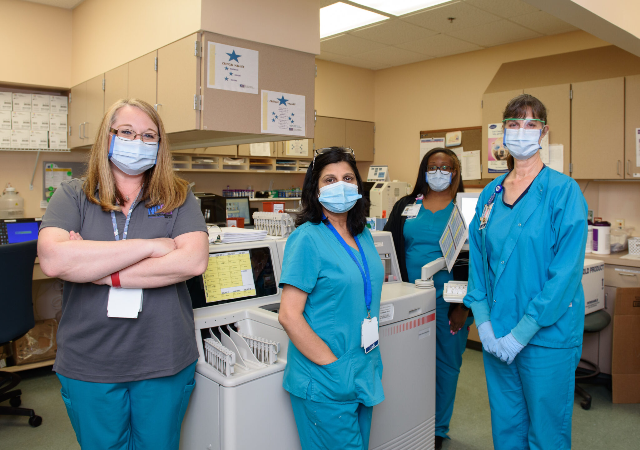Four female staff members in scrubs and masks stand in the office and smile for the camera.

