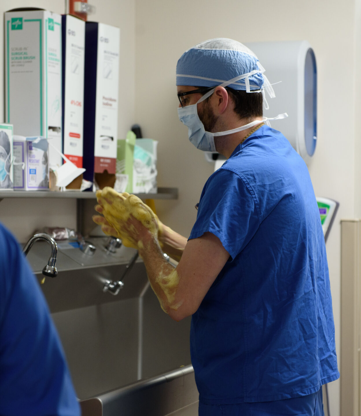  A staff member in scrubs and a mask washes their hands. 