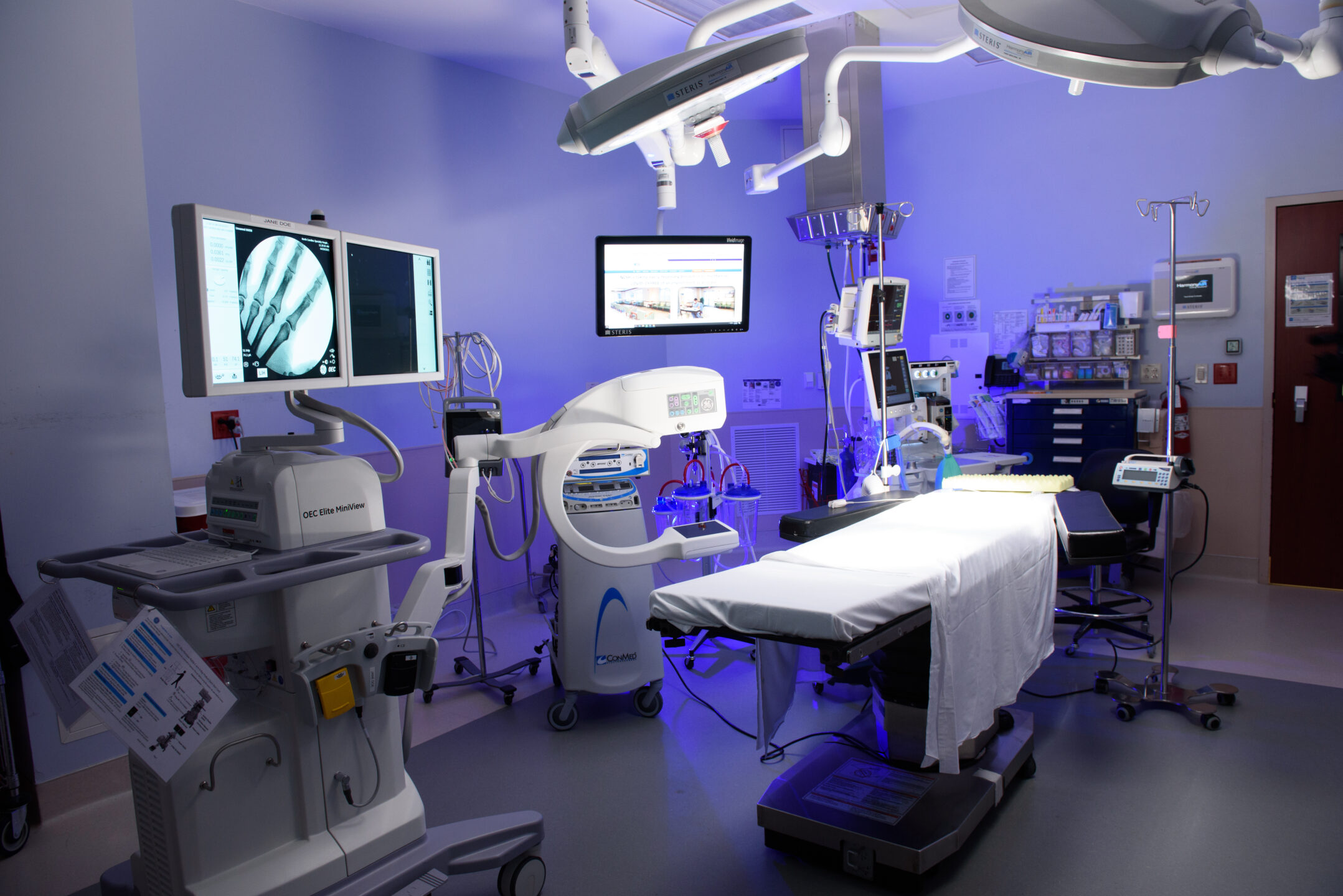 A surgery room with bed, equipment, and X-ray images is lit with blue light. 