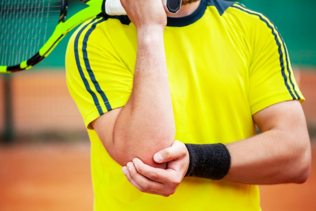 A tennis player in a yellow shirt holds his injured elbow and wonders if he has a Tommy John injury.