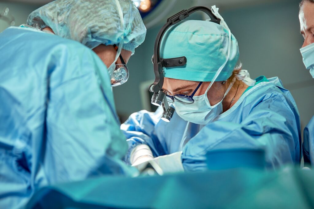 A surgeon leans over a patient with two people assisting.