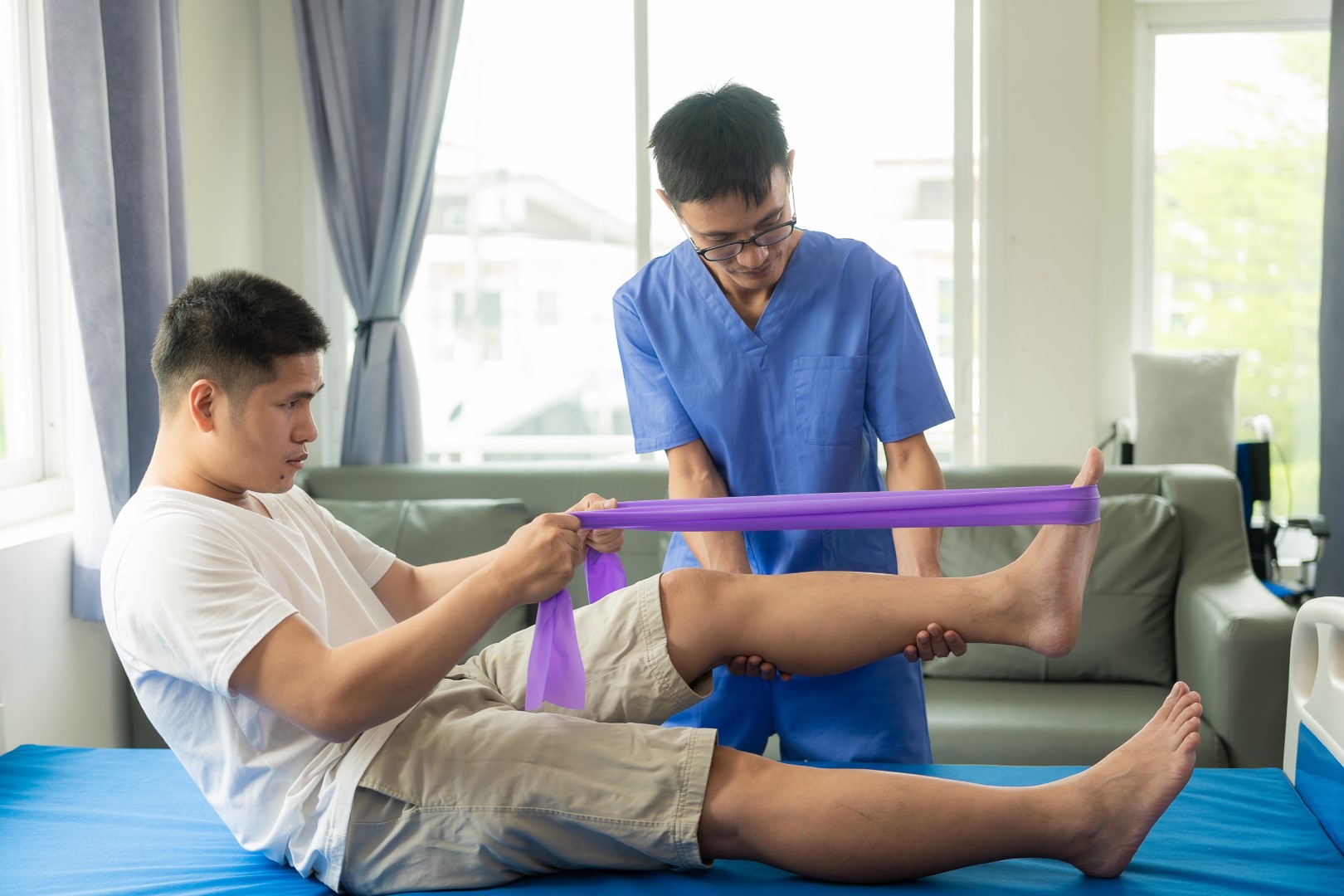A physical therapist supports a patient’s leg as he does an exercise with a resistance band around his foot. 