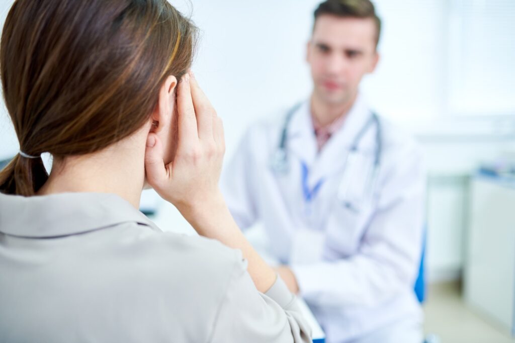 A young woman holding her hand to her ear asks her doctor if her eardrum is ruptured.