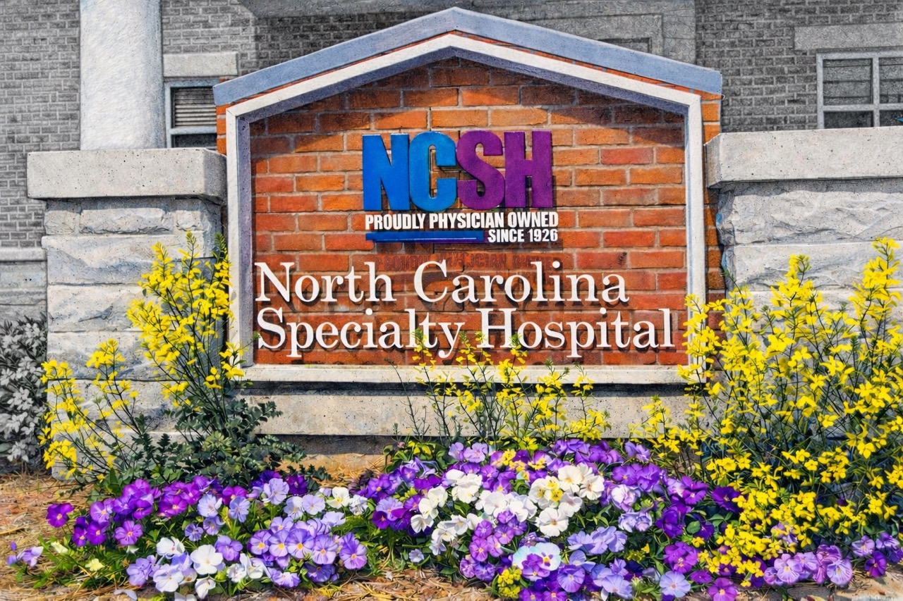 A colorful NCSH sign on red brick surrounded by purple and yellow flowers.