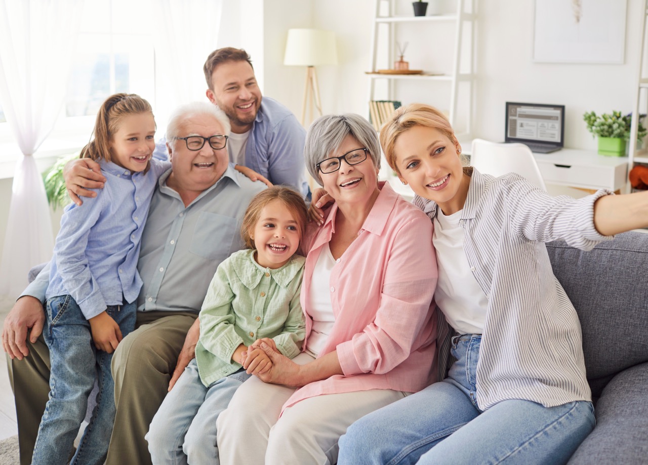 A multi-generational family squeezes on a couch to take a selfie.