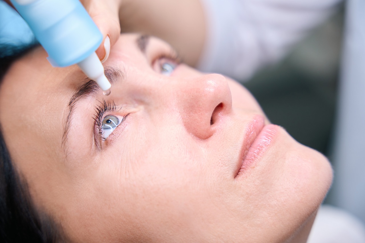 A close-up photo of a woman’s face shows an ophthalmologist putting drops in the patient’s eyes to dilate the pupils for a retinal exam for diabetes.