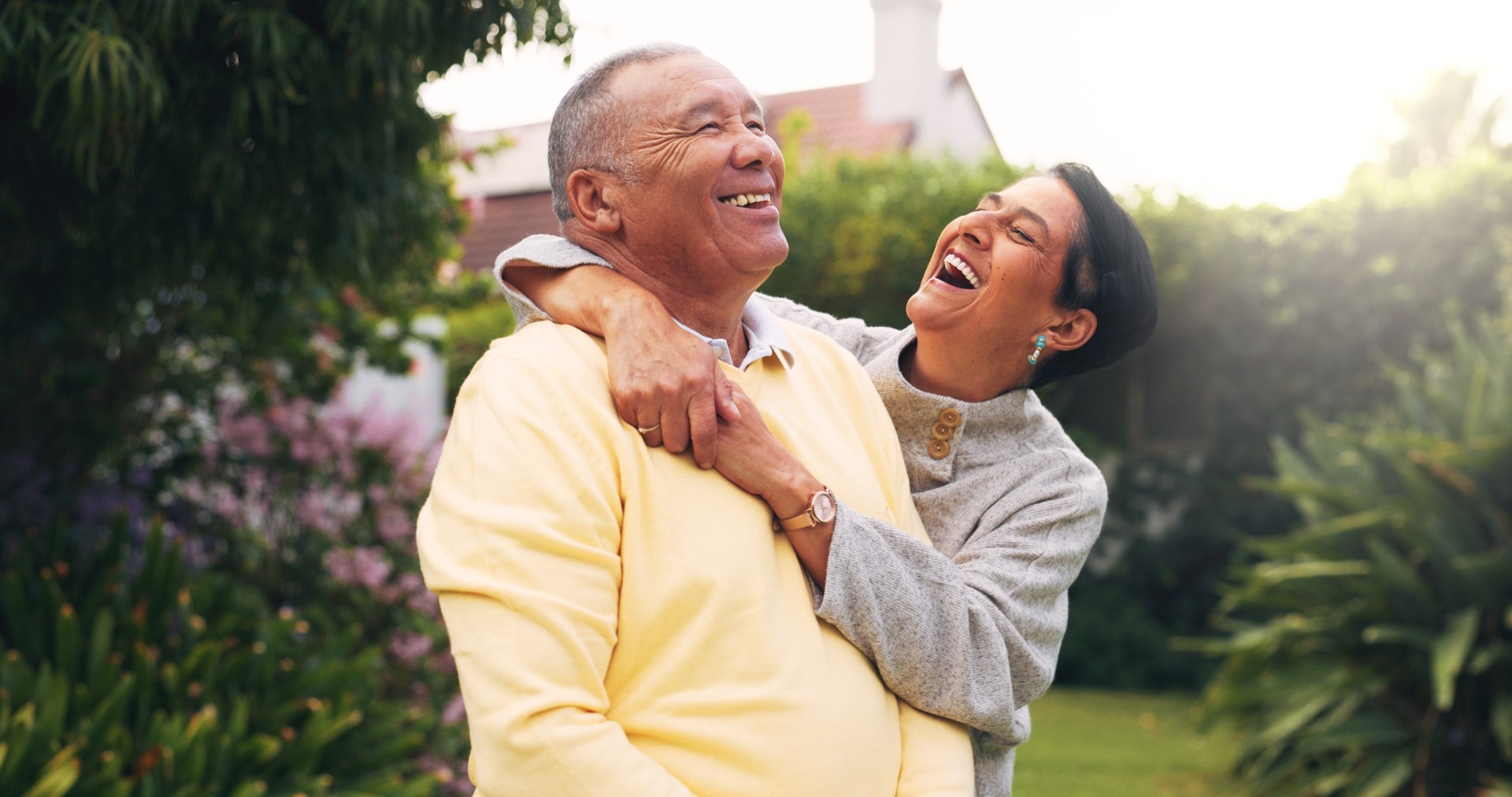 A happy, active couple outside as the wife hugs her husband from behind.
